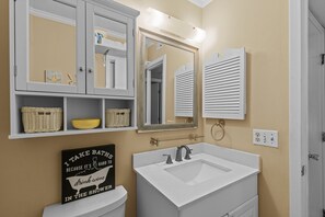 A bathroom with a white sink, mirror, and shelves with baskets and toiletries. - SUMMER DEAL! PRICE DROP ON THIS GORGEOUS CONDO! ENJOY ALL THE AMENITIES! (Atlantic Beach)