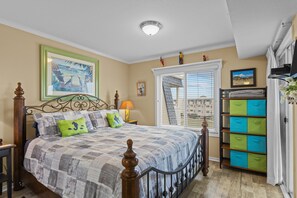 A bedroom with a bed, a nightstand, a lamp, a window with blinds, a staircase, and a storage unit. - SUMMER DEAL! PRICE DROP ON THIS GORGEOUS CONDO! ENJOY ALL THE AMENITIES! (Atlantic Beach)