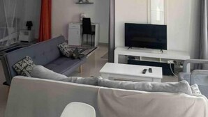 Ein modernes Wohnzimmer mit einer Couch, einem Couchtisch, einem Fernseher auf einem Schrank und einer Deckenleuchte.