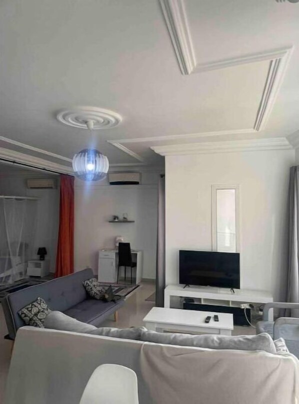 A modern living room with a sofa, a coffee table, a TV on a stand, and a ceiling light.