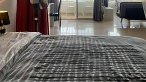 Ein modernes Hotelzimmer mit einem großen Bett, einem Deckenventilator und Meerblick durch große Fenster.