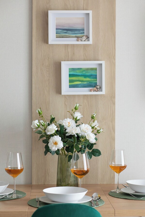 Une table à manger ornée d’un vase de fleurs blanches, de deux verres à vin et d’une assiette.