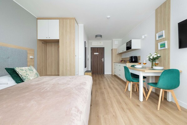 A modern hotel room with a bed, a desk, and a kitchenette.