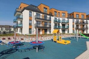 A playground with swings and climbing structures, surrounded by modern apartment buildings with balconies.