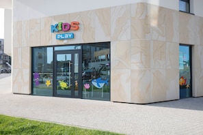 Un bâtiment sur lequel on peut lire l’inscription « ESPACE DE JEUX POUR ENFANTS », avec une entrée en verre décorée de motifs de poissons de dessins animés.