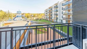 A balcony with a view of a modern apartment building, a playground, and a water slide.