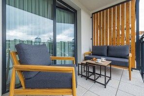 Een balkon met twee houten stoelen, een klein tafeltje met een kopje en gebak, en uitzicht op een gebouw met een koepel.