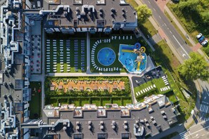 An aerial view of a modern building with a rooftop garden, a swimming pool, and a parking lot.