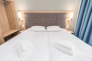 A double bed with two pillows, a wooden headboard, bedside lamps, and a blue curtain.