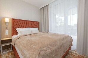 A hotel room with a bed, a nightstand, a lamp, and a window with curtains. - Modern Apartment | Balcony, Parking, Close to the Beach (Międzyzdroje)