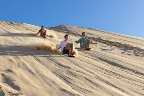 Una pendiente arenosa con tres personas deslizándose cuesta abajo.