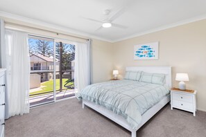 Ein Schlafzimmer mit einem Bett, zwei Nachttischen inklusive Lampen, einem Deckenventilator, einer Schiebeglastür, die auf einen Balkon führt, und einem Wandbild mit einem Fischmotiv.