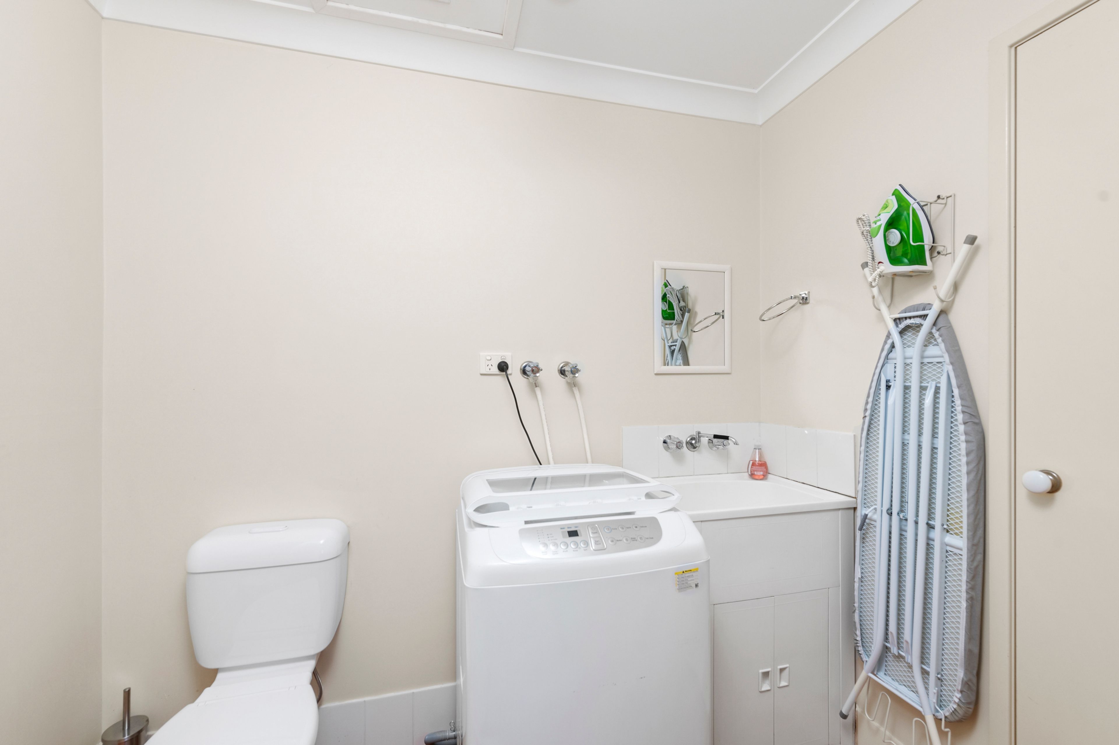 Un baño con inodoro, lavadora y tendedero.