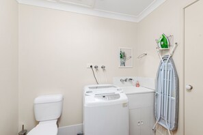 A bathroom with a toilet, a washing machine, and a drying rack. - Sandcastles Anna Bay House Near The Ocean (Anna Bay)