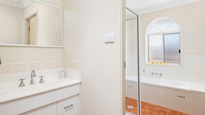 Un baño con tocador blanco, espejo, ventana con vistas y zona de ducha.