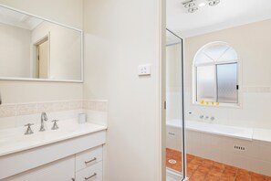 Ein Badezimmer mit weißem Waschtisch, einem Spiegel, einem Fenster mit Aussicht und einer Duschkabine.