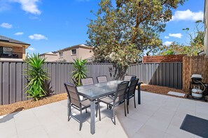 A patio with a glass-top table and chairs, surrounded by a wooden fence and a tree. - Sandcastles Anna Bay House Near The Ocean (Anna Bay)