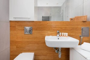 A modern bathroom with a wooden accent wall, a white sink with multiple toiletries, and a visible towel rack.