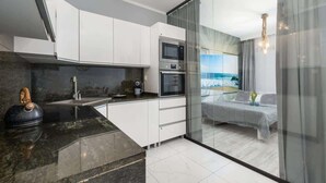 A modern kitchen with white cabinets, a black countertop, and a view of a balcony with a bed and curtains. - Stylish Apartment with Balcony | Parking | Close to the Beach (Kolobrzeg)