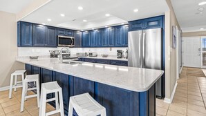 A modern kitchen with blue cabinets, stainless steel appliances, and a large island with bar stools. - Condo with Private Balcony & Beach Views Near Pier (Garden City Beach)