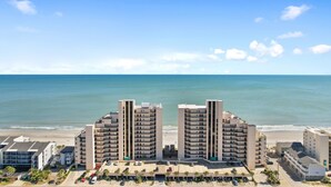 A beachfront hotel with two tall buildings, a parking lot, and a beach in the background. - Condo with Private Balcony & Beach Views Near Pier (Garden City Beach)