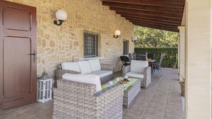 Ein überdachter Patio-Bereich mit Korbmöbeln, Steinwänden und einer Holzbalkendecke.