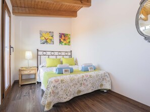 A bedroom with a bed, a nightstand, a lamp, and two flower paintings on the wall. - Villa Las Comas de Dalt · 4 bedrooms (Alcúdia)