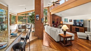 A spacious living area with a high ceiling, a brick fireplace, and a television.