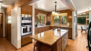 A modern kitchen with wooden cabinets, stainless steel appliances, a granite countertop, and a large window providing natural light.