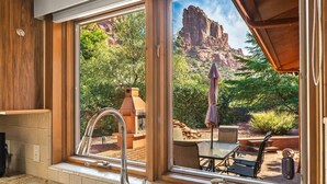 A kitchen with a large window overlooking a patio with a barbecue grill and outdoor furniture.