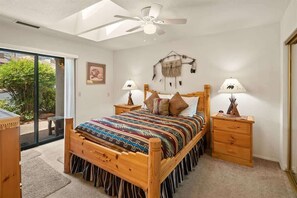 A bedroom with a bed, two bedside tables, a ceiling fan, a window, and a door leading to a balcony.