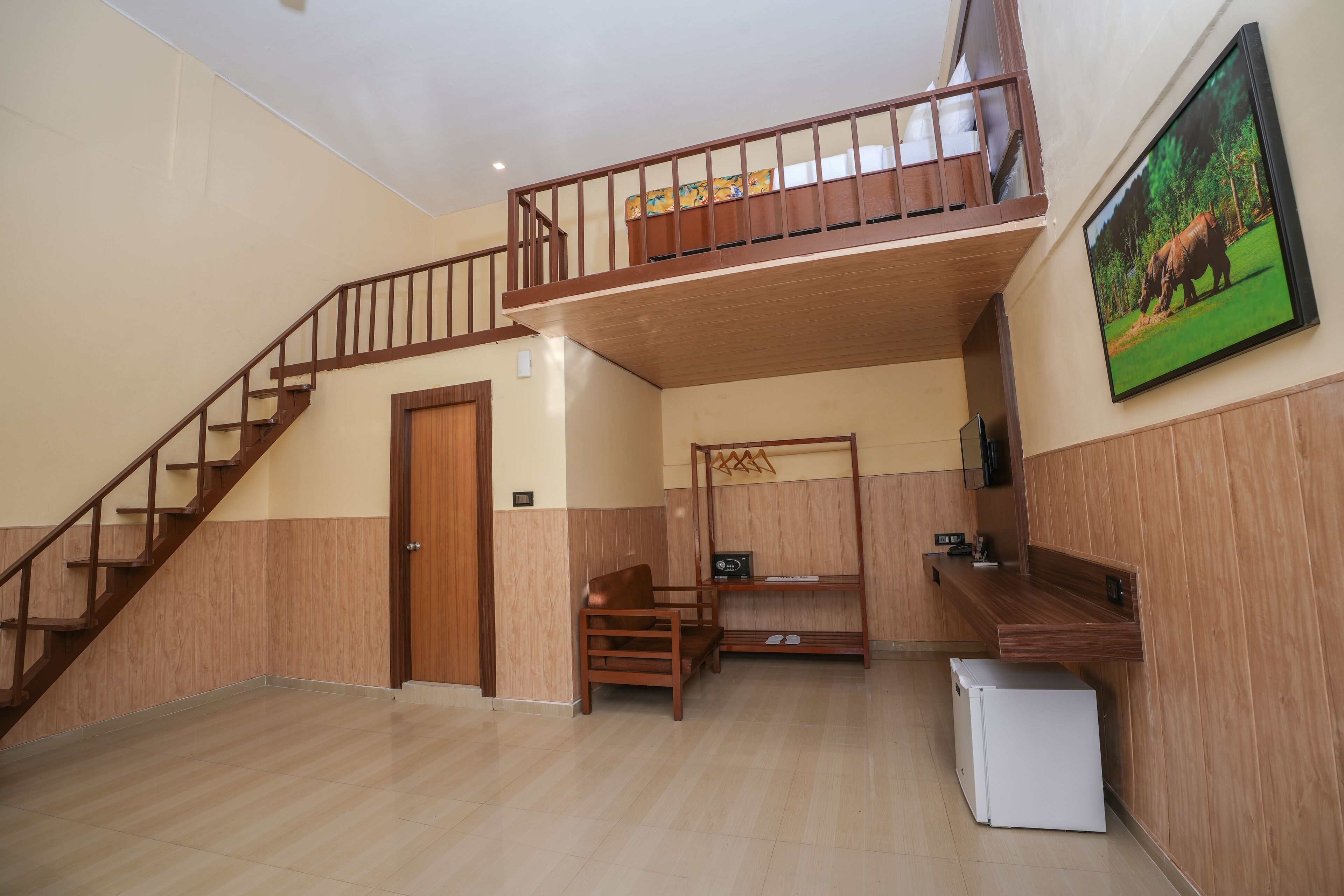 Une pièce spacieuse avec un escalier en bois, un lit superposé, un petit réfrigérateur et un téléviseur fixé au mur.