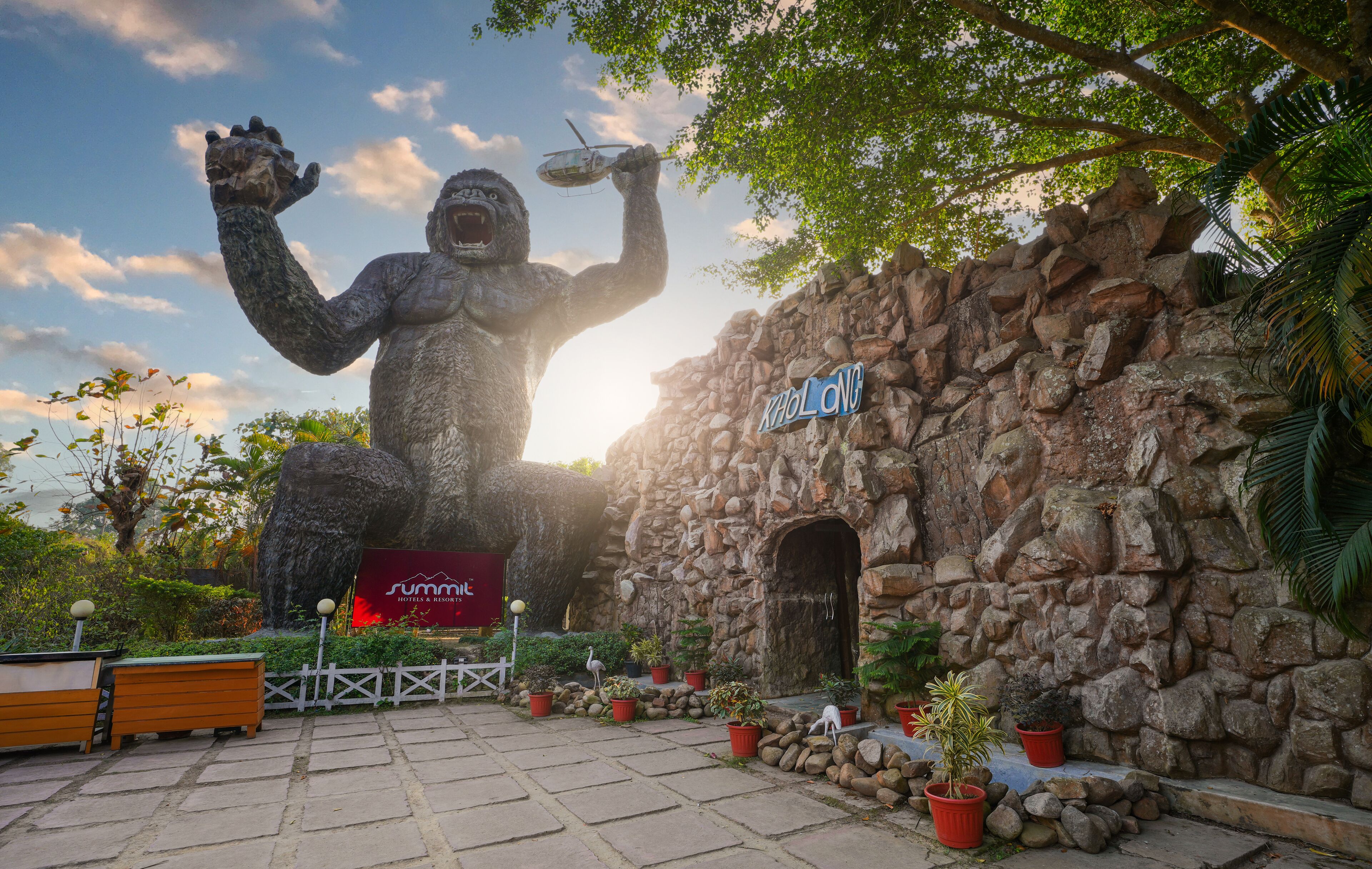 A large gorilla statue holding a plate, a stone wall, and a sign that reads "Khao Long".