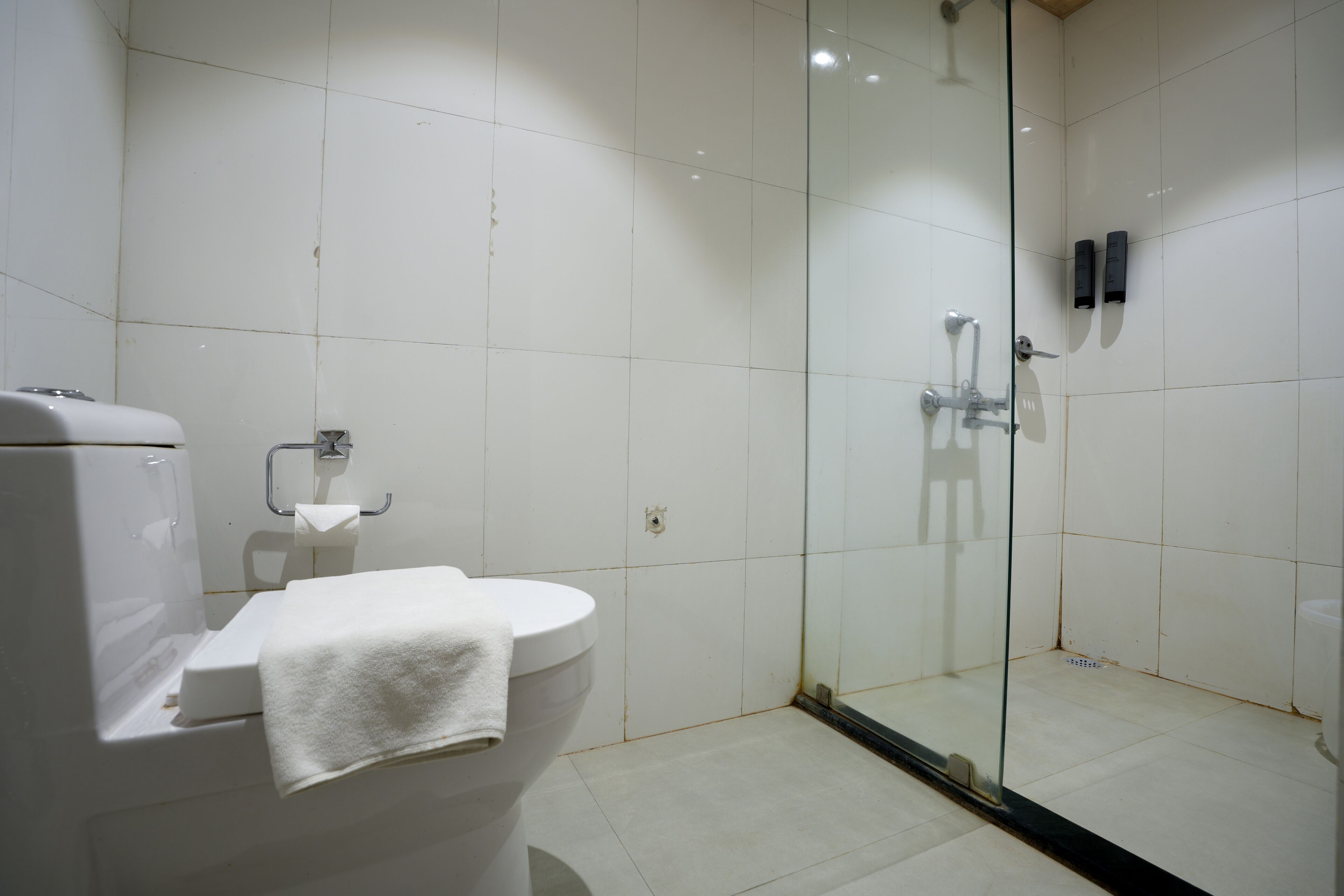 A bathroom with a toilet, a glass-enclosed shower, and white tiled walls.