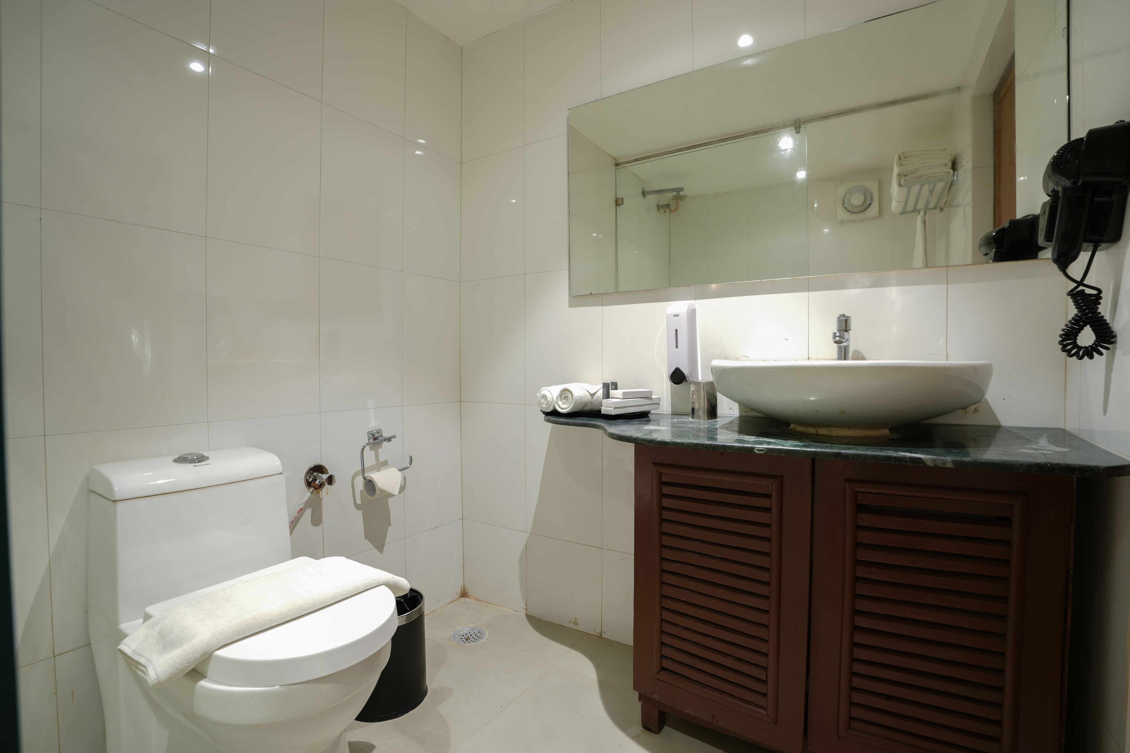 A modern bathroom with a white toilet, a sink with a large mirror above it, and a brown cabinet.