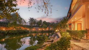 Una tranquilla location di un hotel sul lago, con il riflesso del cielo, un giardino curato e un edificio con un balcone affacciato sull'acqua.