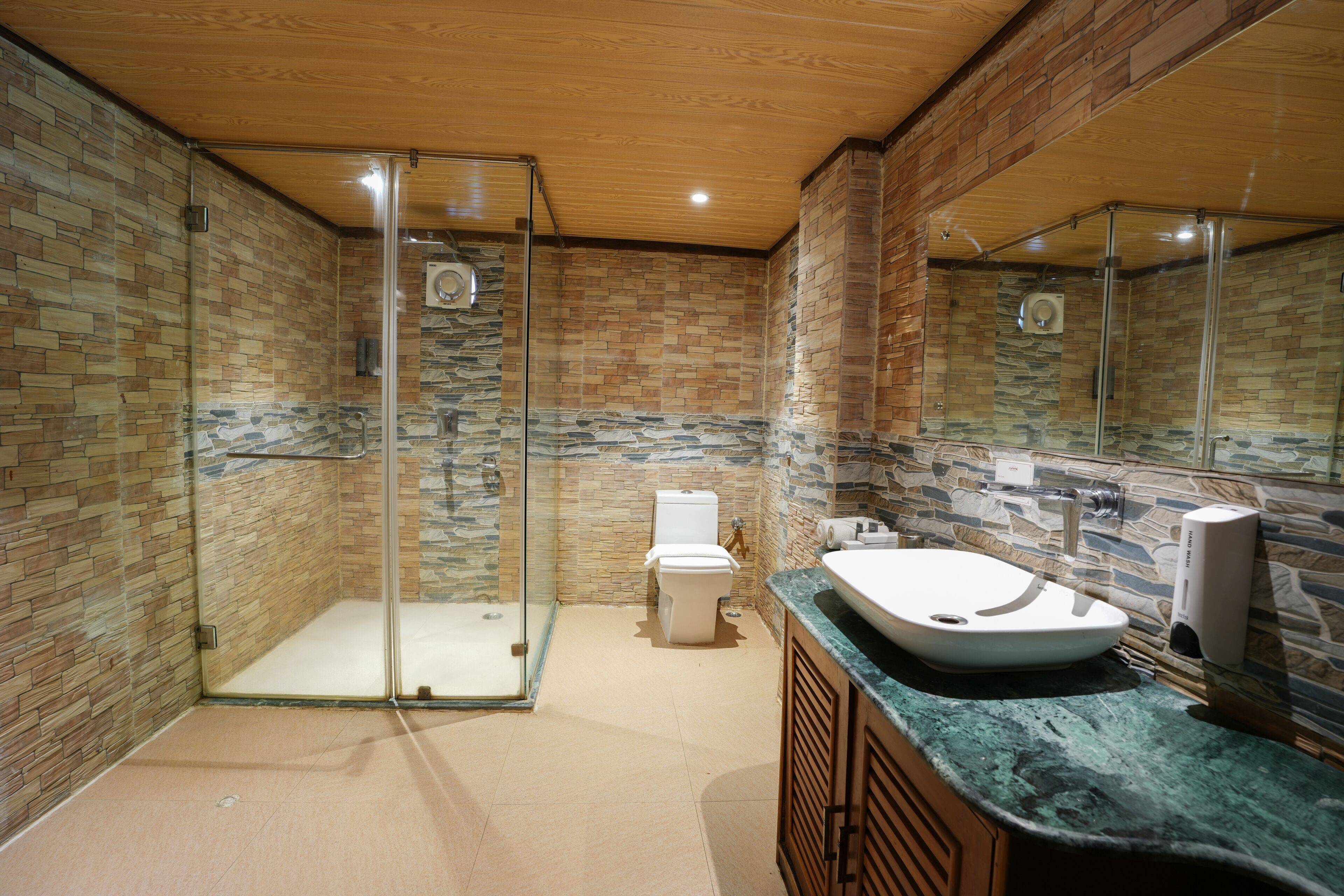Een moderne badkamer met een douche in een glazen cabine, een wit toilet en een ruime wastafel met een aanrechtblad van natuursteen.