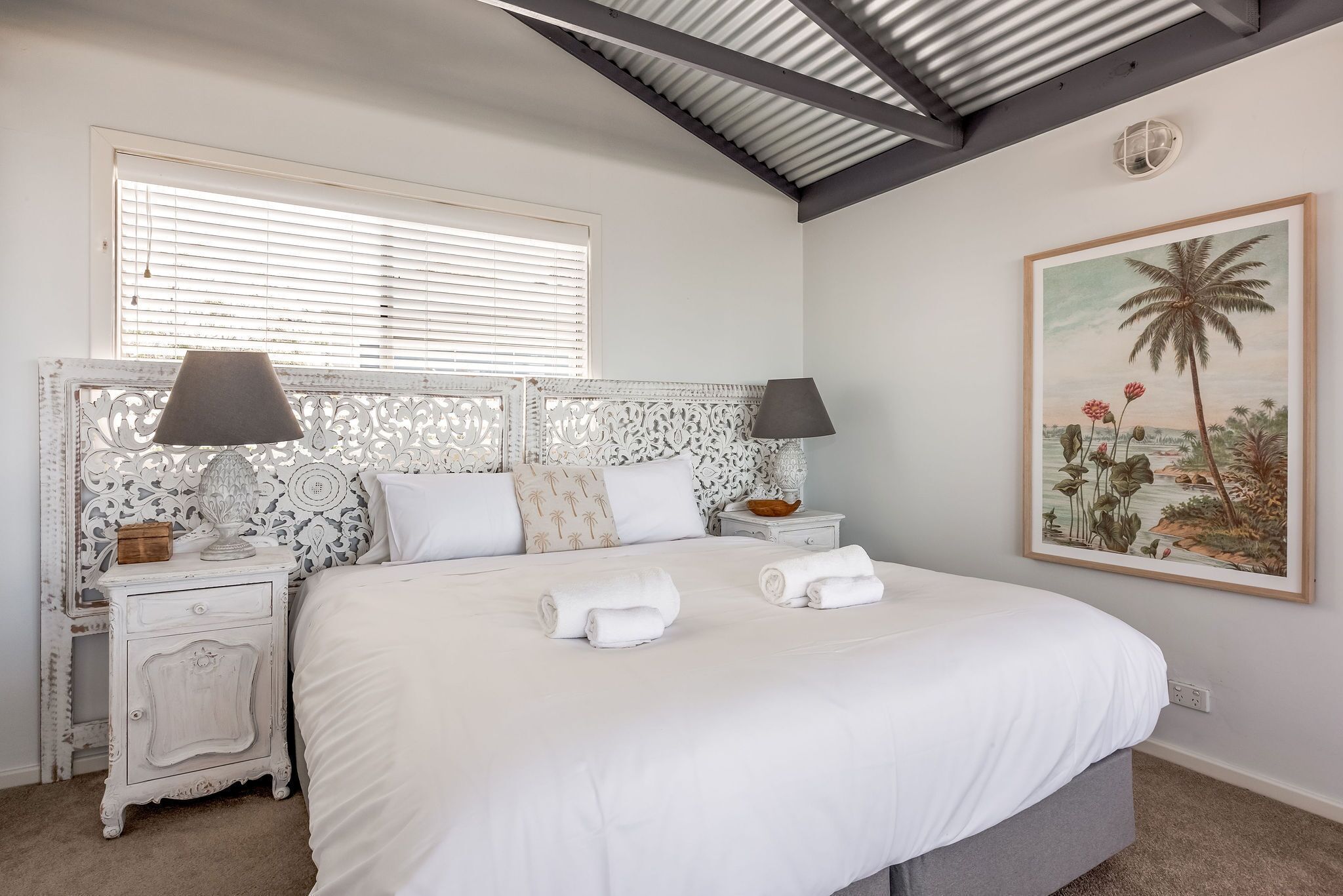 Una camera da letto con un letto grande, due comodini con lampade, una testiera decorativa, una finestra con tende e un quadro appeso al muro.
