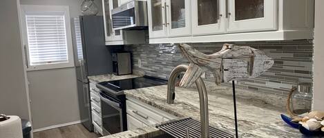 Et moderne køkken med lyse skabe, et rustfrit stål køleskab, indbygget ovn og en marmor bordplade.