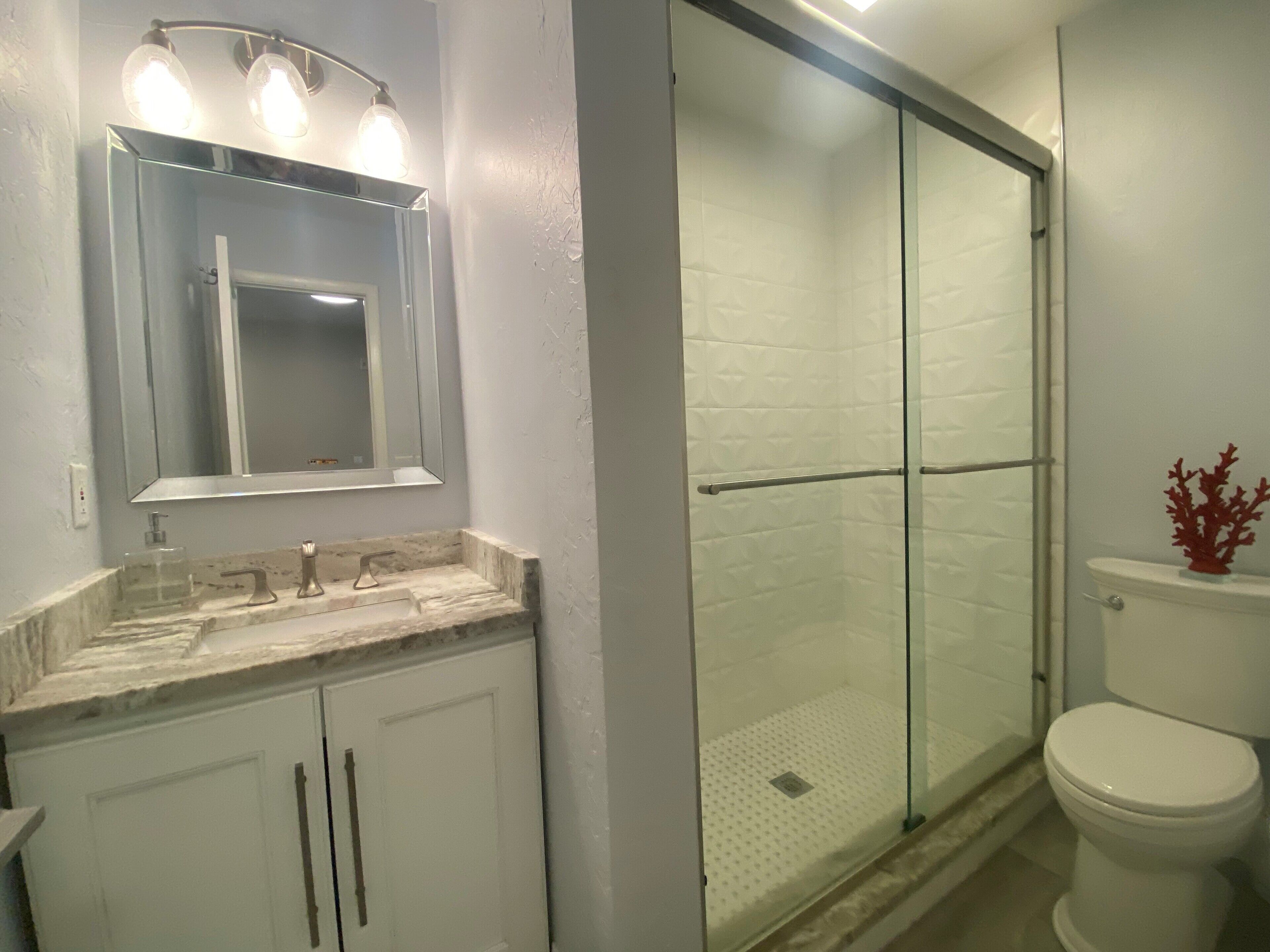 A bathroom with a glass shower enclosure, a white toilet, and a marble sink with a mirror above.