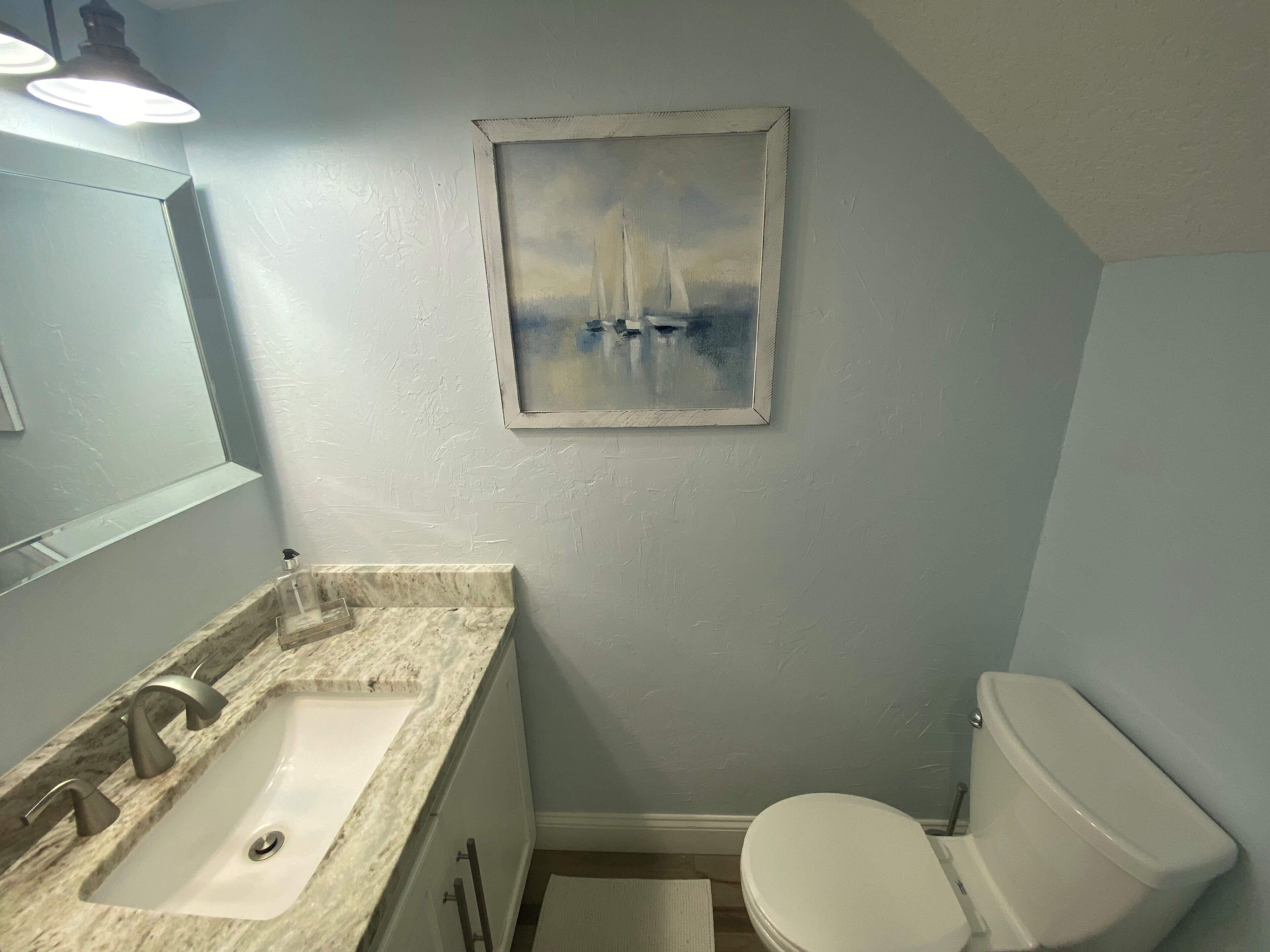 Un baño con lavamanos de mármol, inodoro blanco y un cuadro de veleros en la pared.