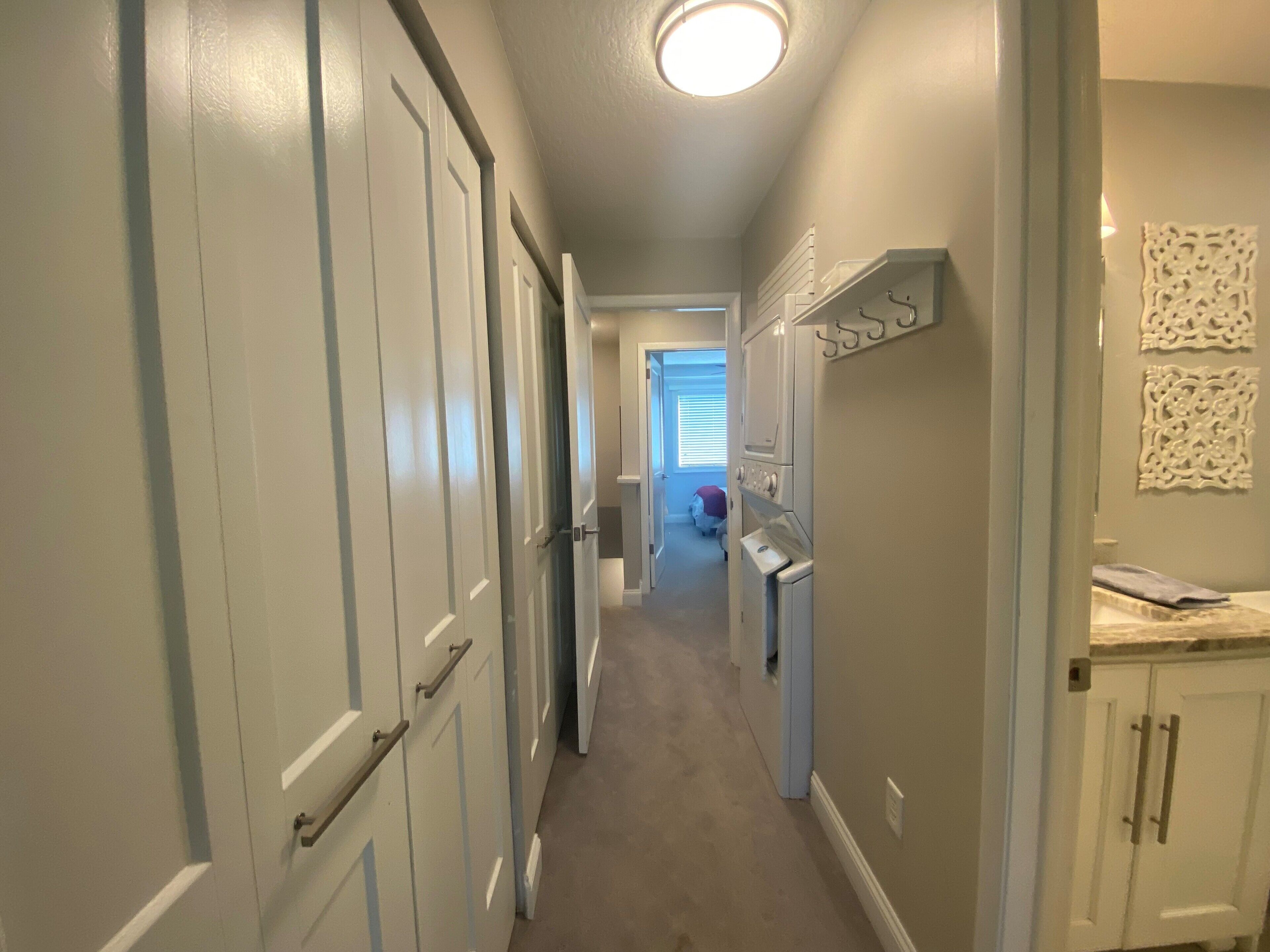 Un couloir étroit avec des portes blanches, un luminaire au plafond et un petit coin cuisine équipé de placards et d’un plan de travail.