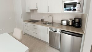 A modern kitchen with white cabinets, a stainless steel microwave, a coffee maker, and a dishwasher. - Apartamento Idaira Sun (Los Cristianos)