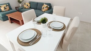 A modern dining area with a white table set for two, surrounded by a green sofa and a small coffee table. - Apartamento Idaira Sun (Los Cristianos)