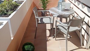 A small outdoor balcony with a table and chairs, a potted plant, and a view of the cityscape. - Apartamento Idaira Sun (Los Cristianos)