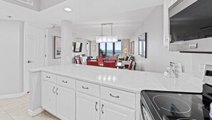 Una cocina moderna con armarios blancos, una estufa negra y una zona de comedor con sillas rojas.