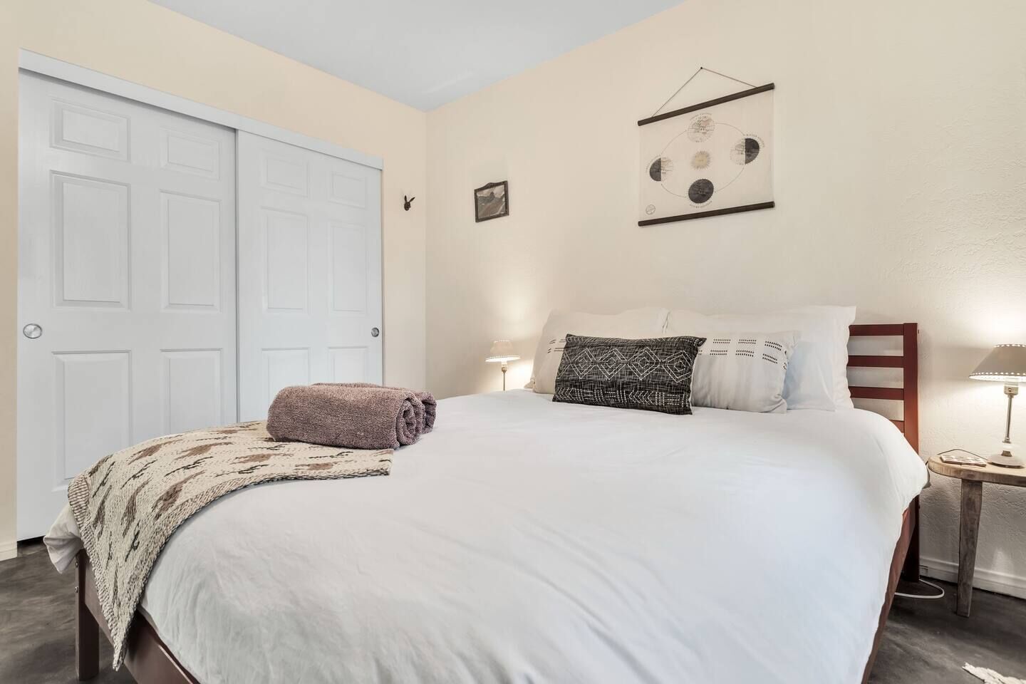 A neatly made bed with a patterned throw blanket and pillows, a bedside lamp, and a framed picture on the wall.