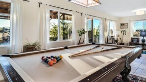A pool table with balls, a hanging lamp, and windows with curtains. - Dez-Art Retreat - Eclectic Getaway near JTNP (Yucca Valley)