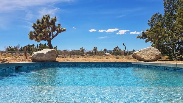 A clear blue pool surrounded by desert landscape and large rocks. - Dez-Art Retreat - Eclectic Getaway near JTNP (Yucca Valley)