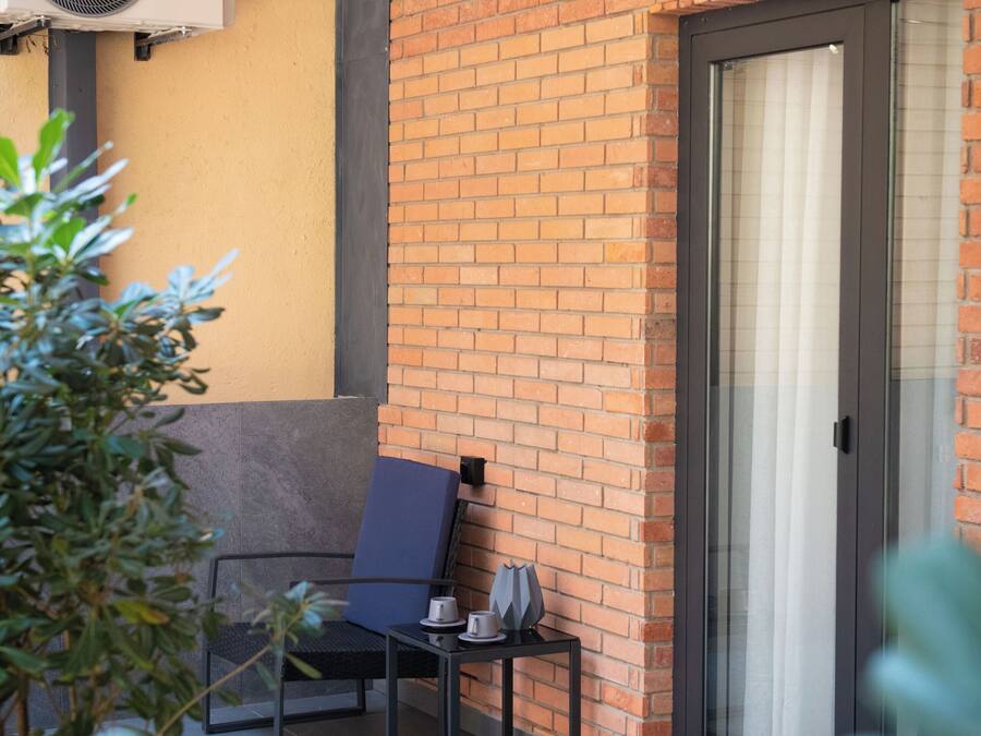 An outdoor seating area with a brick wall, two air conditioning units, a door, and potted plants.